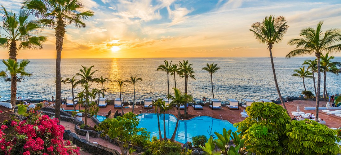 Blick über eine Gartenanlage mit Pool auf das Meer, sonnig