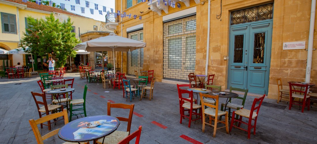 Altstadt von Nikosia: gemütlicher Platz mit Straßencafé, bunten Stühlen, Sandsteinfassaden und Wimpelketten.