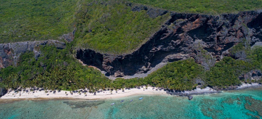 Drohnenaufnahme der Steilküste Los Haitises mit dem Playa Frontón in der Dominikanischen Republik mit dichter grüner Vegetation, dunklen Felsformationen, weißem Sandstrand und türkisblauem Wasser