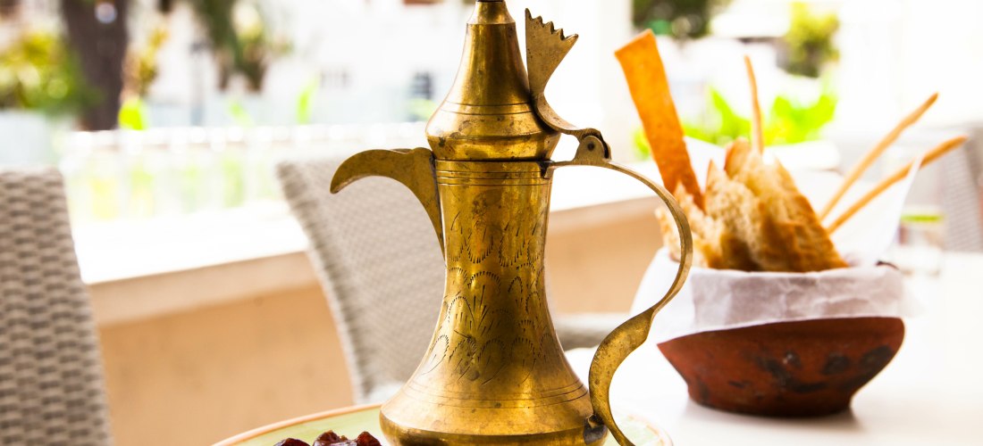 Ramadan, Kaffekanne aus gold auf einem Tisch, mit Datteln und Marshmallows, Brot im Hintergrund.