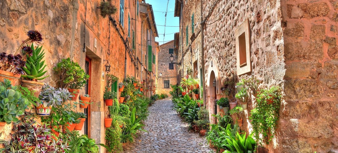 Malerische Gasse in Valldemossa auf Mallorca mit Kopfsteinpflaster, historischen Steinhäusern und vielen Blumentöpfen an den Fassaden