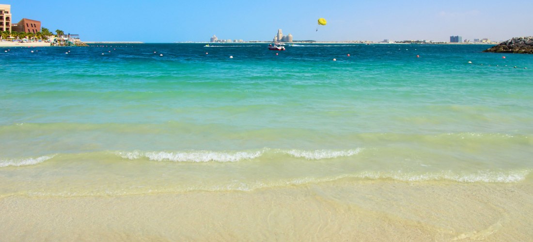 Strand von Ras Al Khaimah mit türkisblauem Meer, Parasailing und Blick auf Hotels – beliebtes Reiseziel in den Vereinigten Arabischen Emiraten.