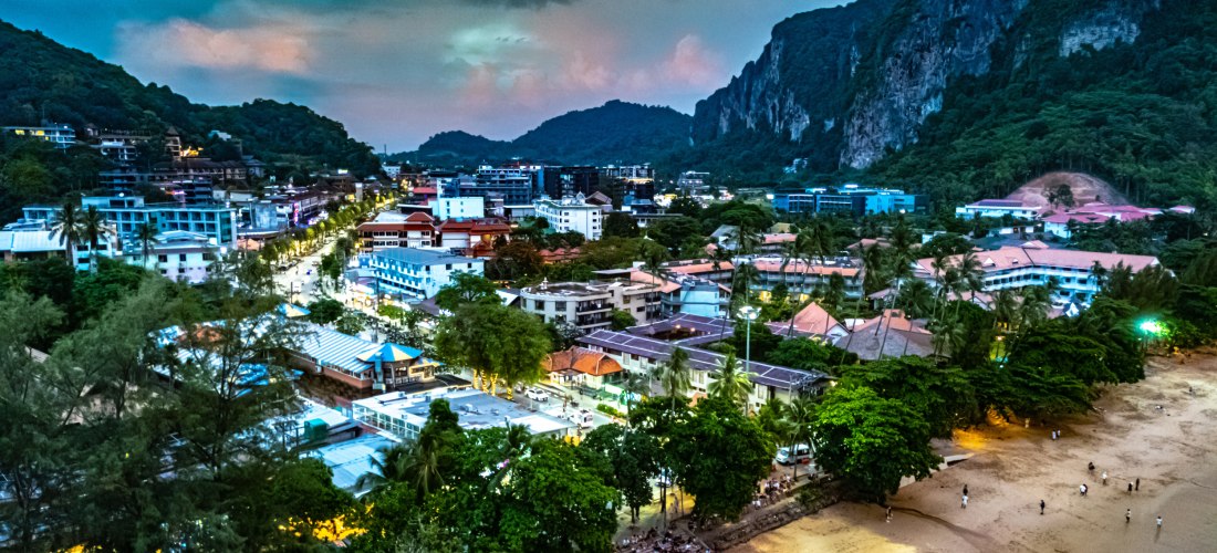 Ao Nang in Krabi bei Abenddämmerung: Lichter der Stadt, belebter Strand und Kalksteinfelsen im Hintergrund.
