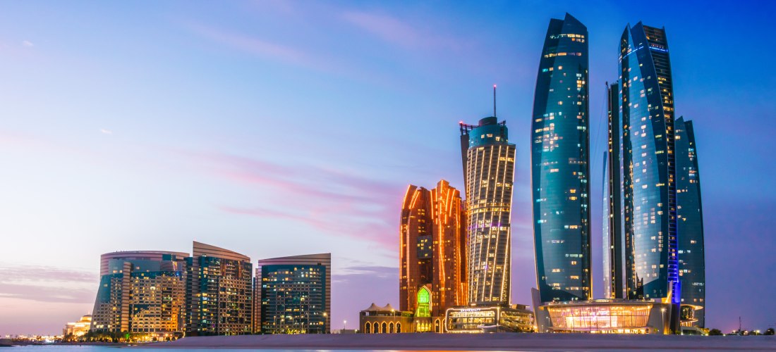 Skyline von Abu Dhabi bei Sonnenuntergang mit den beleuchteten Etihad Towers am Wasser
