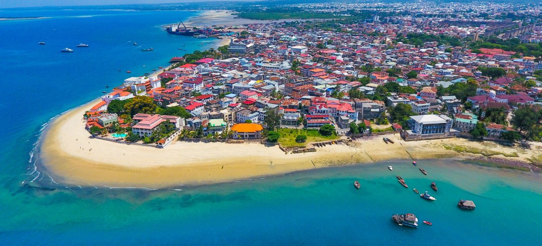 Panorama der Halbinsel von Stone Town, Sansibar: sandige Ufer, rote Dächer der UNESCO-Altstadt und zahlreiche Boote im türkisblauen Wasser