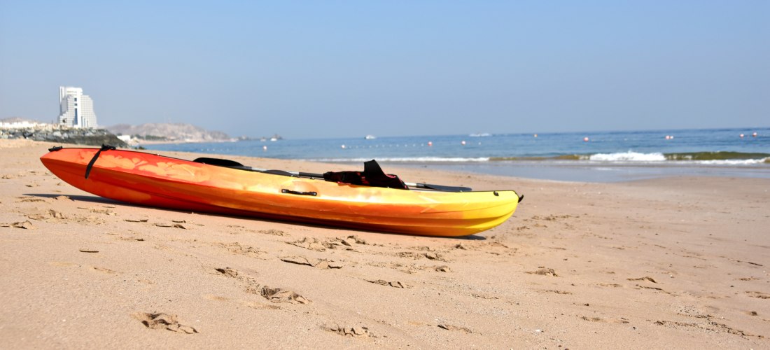 Gelbes Kajak am Strand von Fujairah mit Blick auf das ruhige Meer und die Hotelkulisse. Beliebtes Reiseziel für Badeurlaub und Wassersport in den VAE.