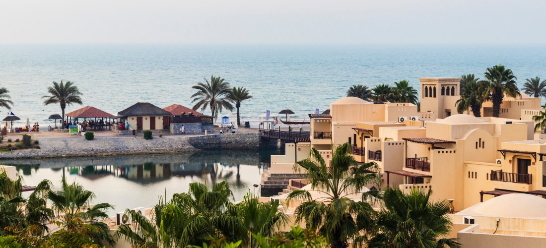 Resort mit traditionellen Sandsteinbauten, Palmen und Blick auf das Meer bei Sonnenuntergang