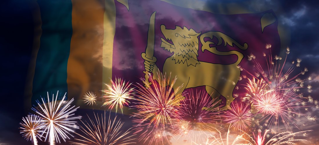 Die Flagge Sri Lankas mit dem goldenen Löwen ist transparent über ein farbenfrohes Feuerwerk am Abendhimmel gelegt.