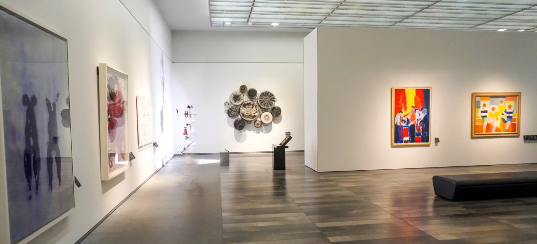 Innenansicht einer modernen Kunstgalerie mit abstrakten Gemälden, Skulpturen und Installationen an weißen Wänden unter einem verglasten Dach