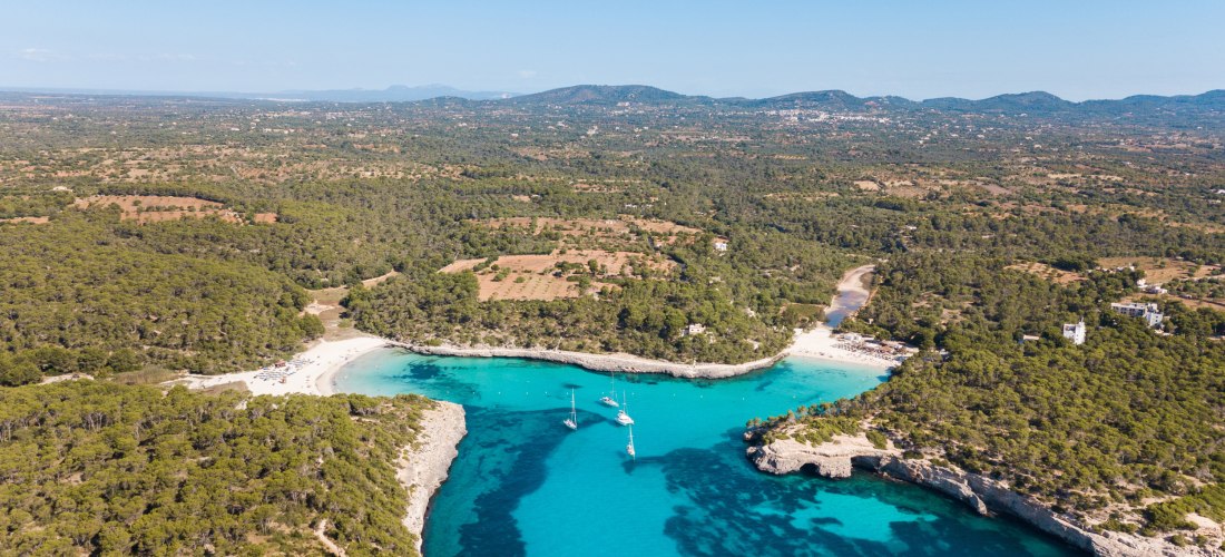 Luftaufnahme von dem Strand von Cala Mondrago auf Mallorca, türkisblaues Wasser, blauer Himmel und Sonnenschein, üppige Vegetation um die Bucht
