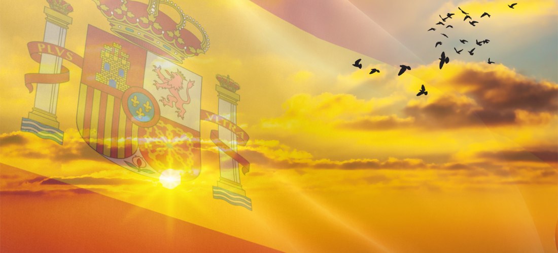 Transparente spanische Flagge mit Wappen weht über einem stimmungsvollen Sonnenuntergang. Der Himmel ist orange-gold gefärbt, einige Wolken sind zu sehen. Rechts fliegt ein Vogelschwarm in Formation.