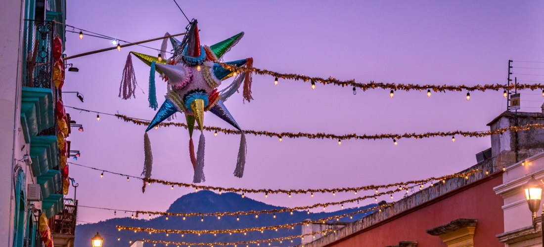 Bunte Weihnachts-Piñata in einer festlich geschmückten Straße mit Girlanden und Lichterketten bei Sonnenuntergang