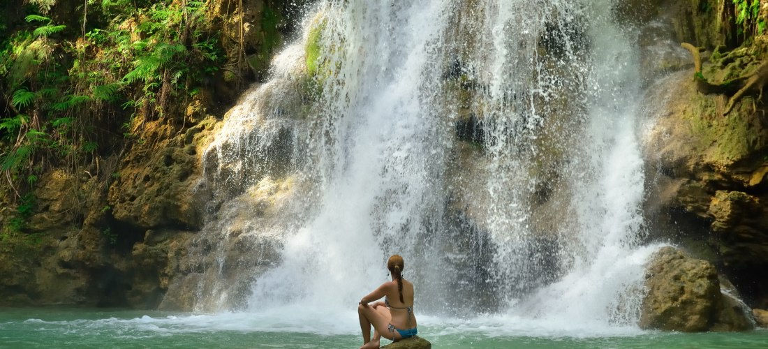 Frau sitzt am Ufer und blickt auf den imposanten Wasserfall El Limón auf Samaná in der Dominikanischen Republik