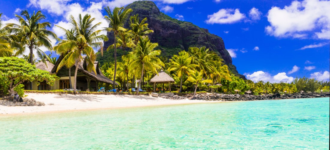 traumhafte tropische Kulisse mit einem luxuriösen Resort direkt am feinen, weißen Sandstrand. Die strohgedeckten Bungalows fügen sich harmonisch in die üppige Landschaft mit hohen, sattgrünen Palmen ein. Das kristallklare, türkisfarbene Wasser schimmert i