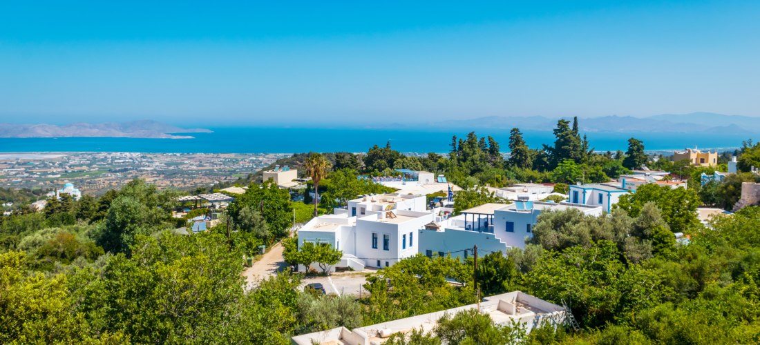 Traditionelle weiße Häuser im Bergdorf Zia auf Kos, eingebettet in grüne Natur mit Blick auf die Küste und das Meer