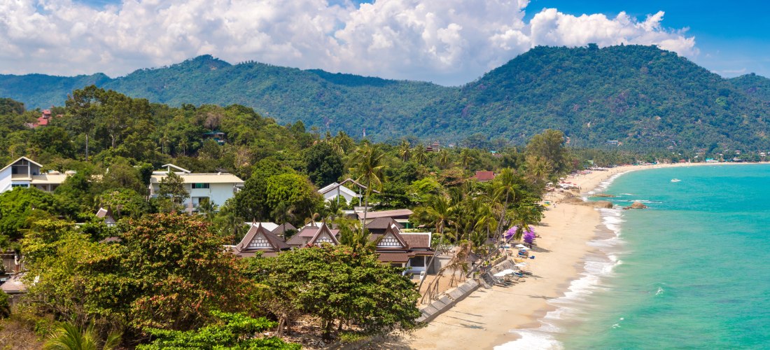 Lamai Beach auf Koh Samui, Thailand: ruhiger Sandstrand mit türkisblauem Wasser, grünen Bergen und kleinen Resorts in tropischer Umgebung.