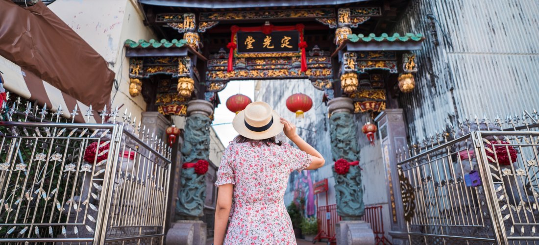 Frau in Sommerkleid steht vor traditionellem chinesischen Tor in Phuket Town, Thailand