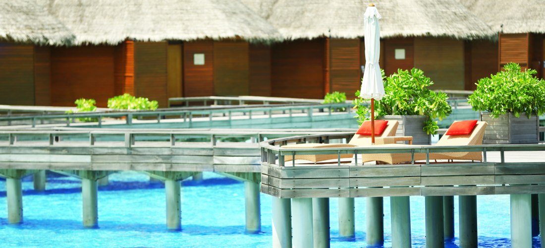 Luxuriöse Wasserbungalows auf den Malediven mit Holzstegen über dem türkisblauen Meer und Sonnenterrassen mit Liegen.