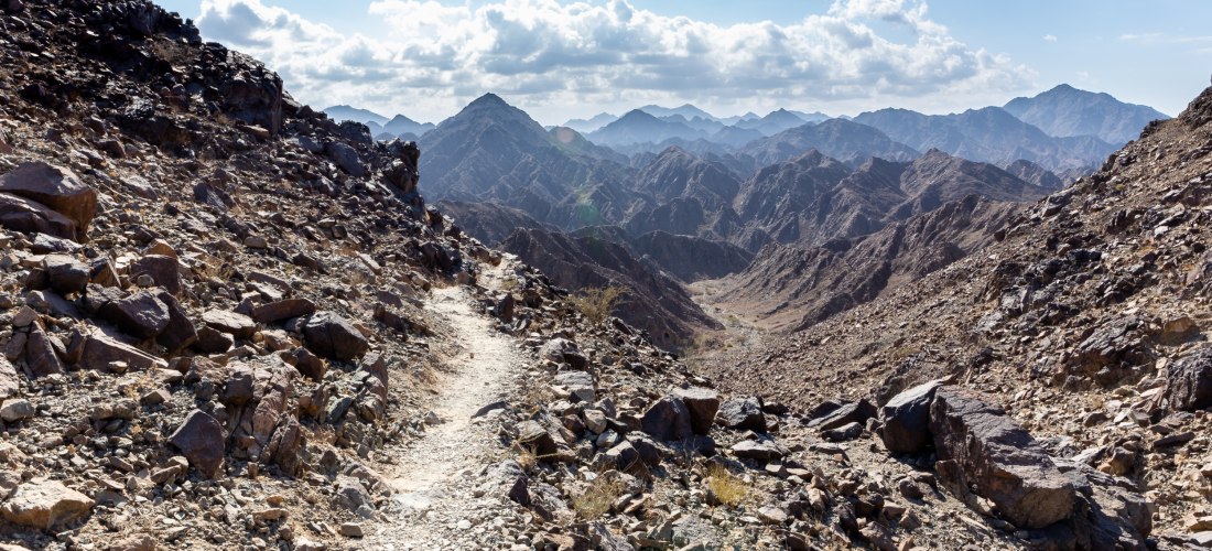 Wanderpfad durch die felsige Berglandschaft des Wadi Shawka in Ras Al Khaimah mit Aussicht auf Gipfelketten.