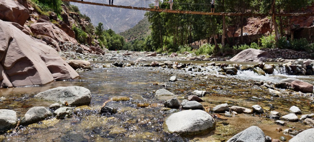 Hängebrücke über einen klaren Gebirgsfluss im Ourika-Tal, Marokko – beliebtes Ausflugsziel mit malerischer Natur und Bergen im Hintergrund.