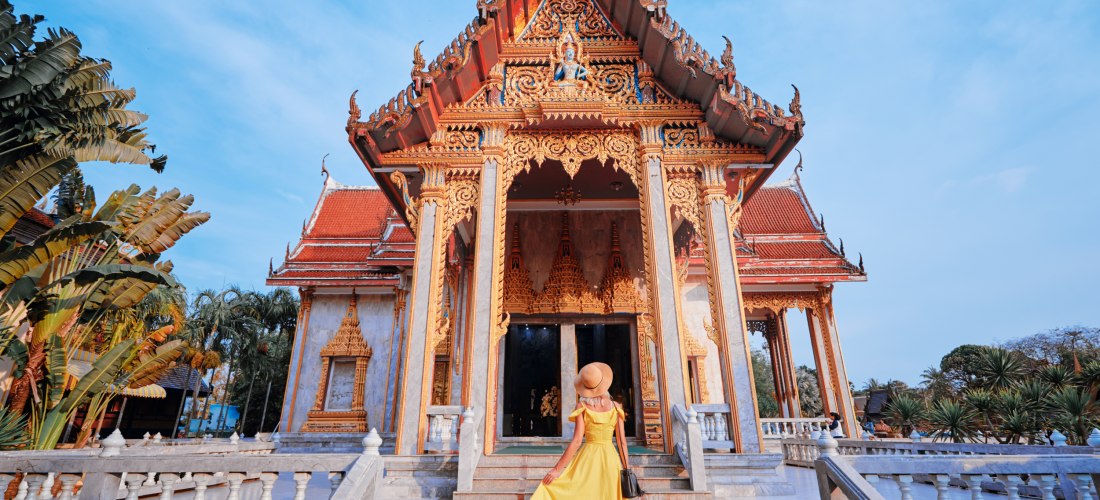 Reisende Frau in gelbem Kleid vor dem Wat Chalong Tempel in Phuket – buddhistische Architektur und kulturelles Highlight Thailands.