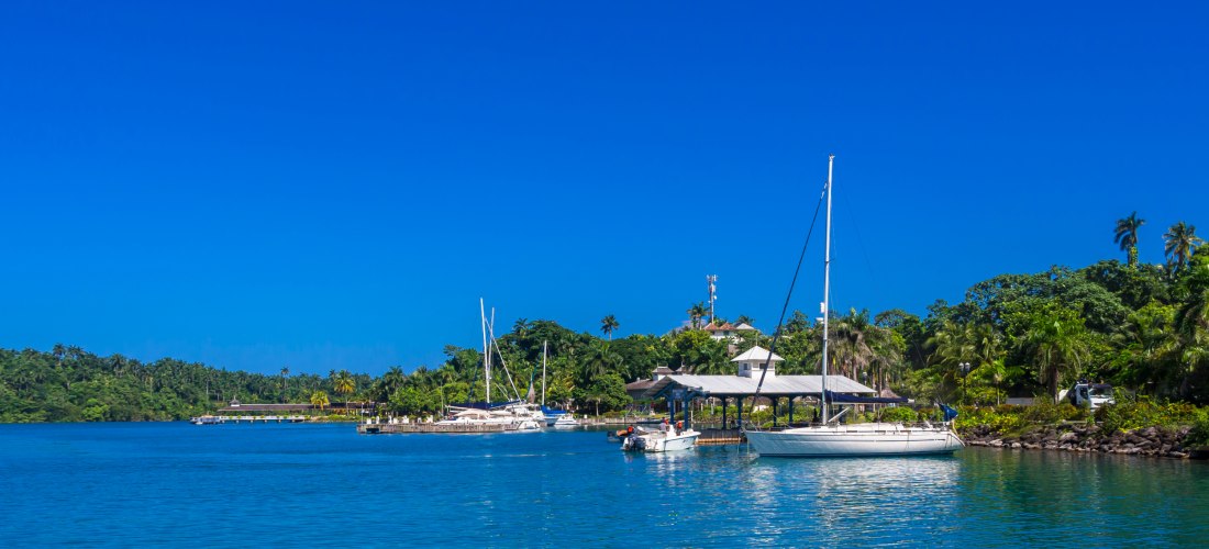 Tropischer Yachthafen mit Segelbooten, türkisblauem Wasser und üppig grüner Landschaft unter strahlend blauem Himmel.