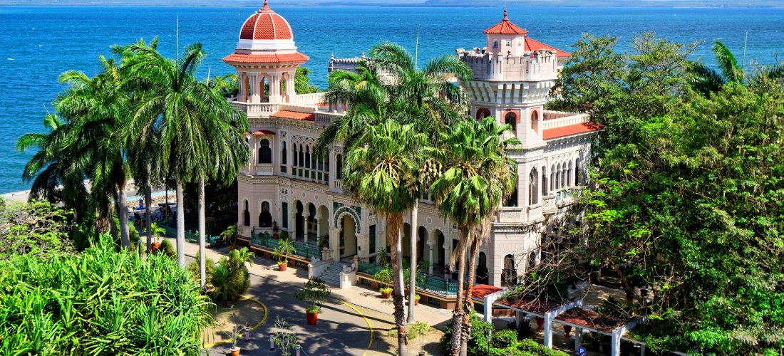 Historische Villa mit roten Kuppeln, umgeben von Palmen, mit Blick auf das Meer