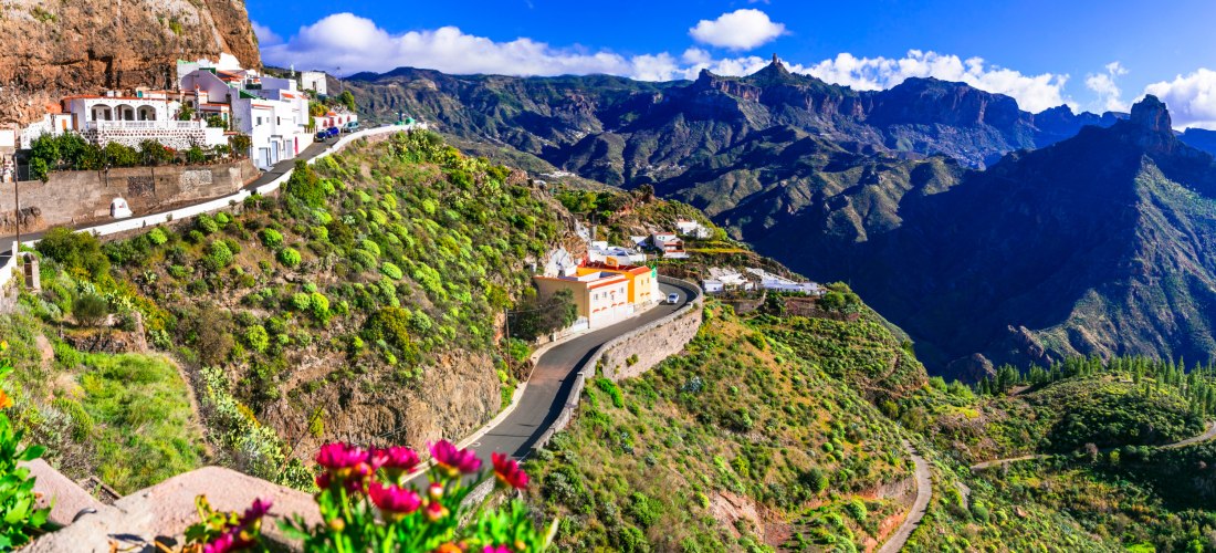 Bergdorf mit weißen Häusern und bunten Fassaden am steilen Hang von Gran Canaria, umgeben von grünen Terrassen und Schluchten.
