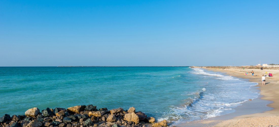 Steinige Küste mit sanften Wellen, türkisfarbenem Wasser und Menschen, die am Strand spazieren