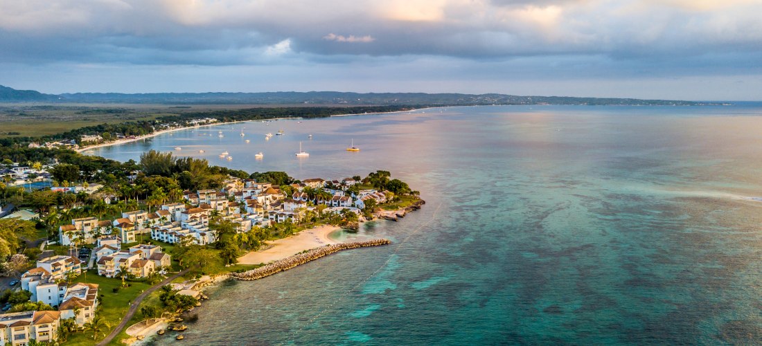 Luftaufnahme der Küste von Negril, Jamaika mit Strand, türkisfarbenem Meer und Resorts bei Sonnenuntergang.