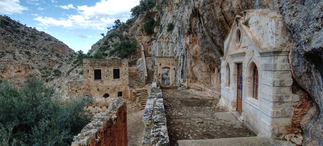 In eine Felswand gebautes Kloster mit kleiner Kapelle, Ruinenmauern und Treppenweg in einer Schlucht