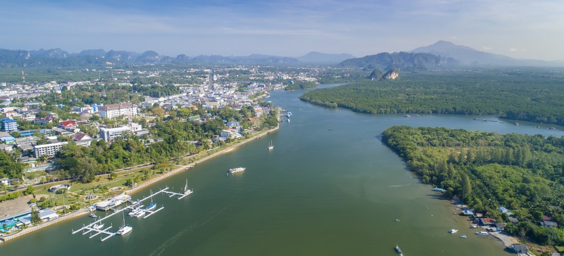 Luftaufnahme von Krabi Town mit Fluss, Hafen, grüner Landschaft und Bergen im Hintergrund in Südthailand.