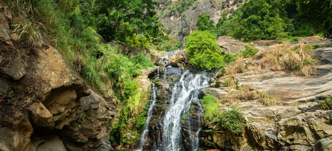 Natürlicher Wasserfall in der Bergregion bei Ella, Sri Lanka, umgeben von Felsen und grüner Vegetation.