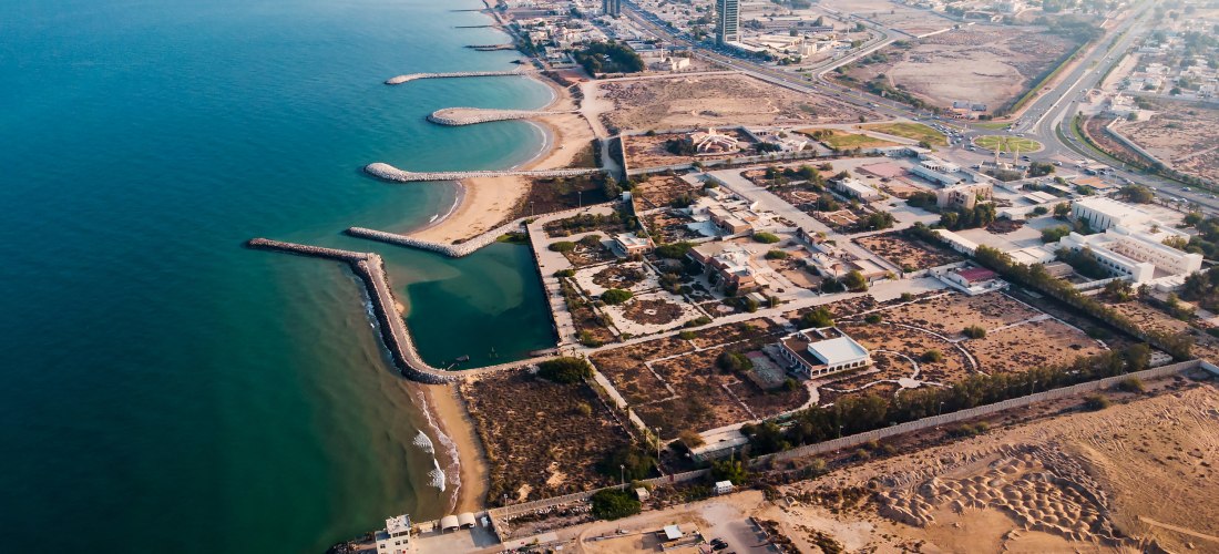 Luftaufnahme der Küste von Ras Al Khaimah mit Sandstrand, Meer und Wellenbrechern.
