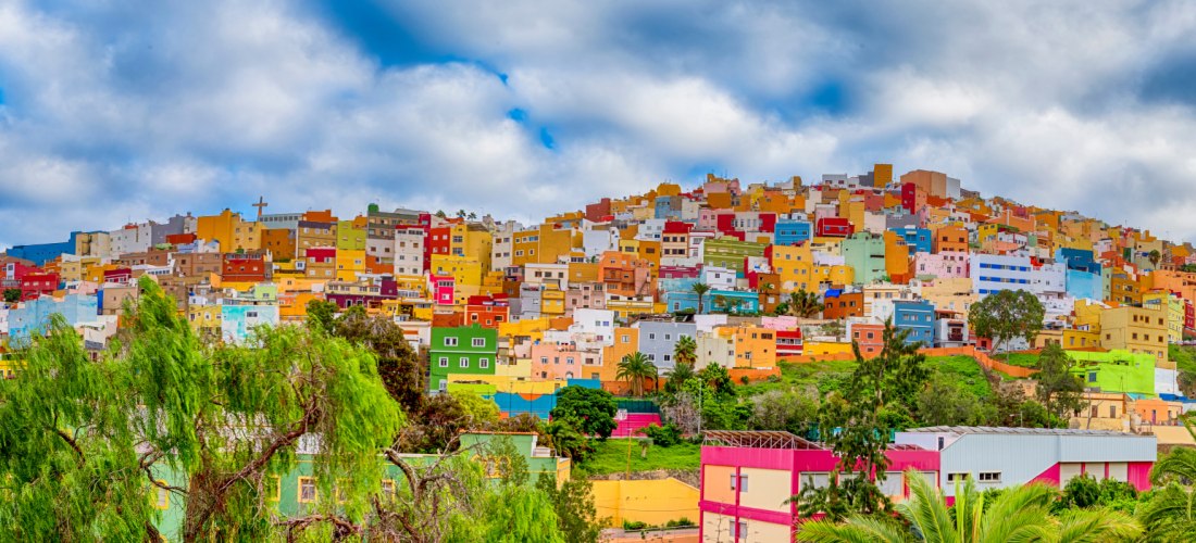 Panorama von Las Palmas de Gran Canaria mit dicht aneinandergebauten bunten Häusern am Hang unter wolkigem Himmel.
