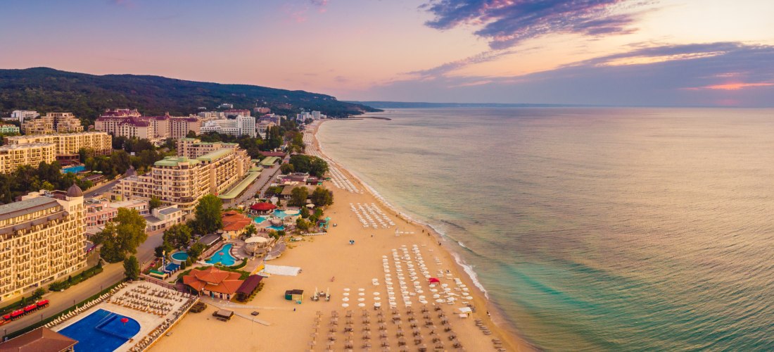 Goldener Sandstrand bei Sonnenuntergang am Goldstrand, Bulgarien, mit Hotels und leeren Sonnenschirmen.