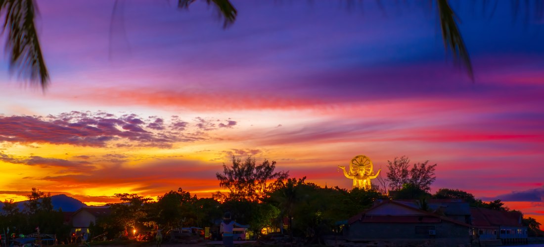 Der Big Buddha Tempel (Wat Phra Yai) auf Koh Samui, Thailand, im farbenprächtigen Sonnenuntergang mit leuchtender goldener Statue.