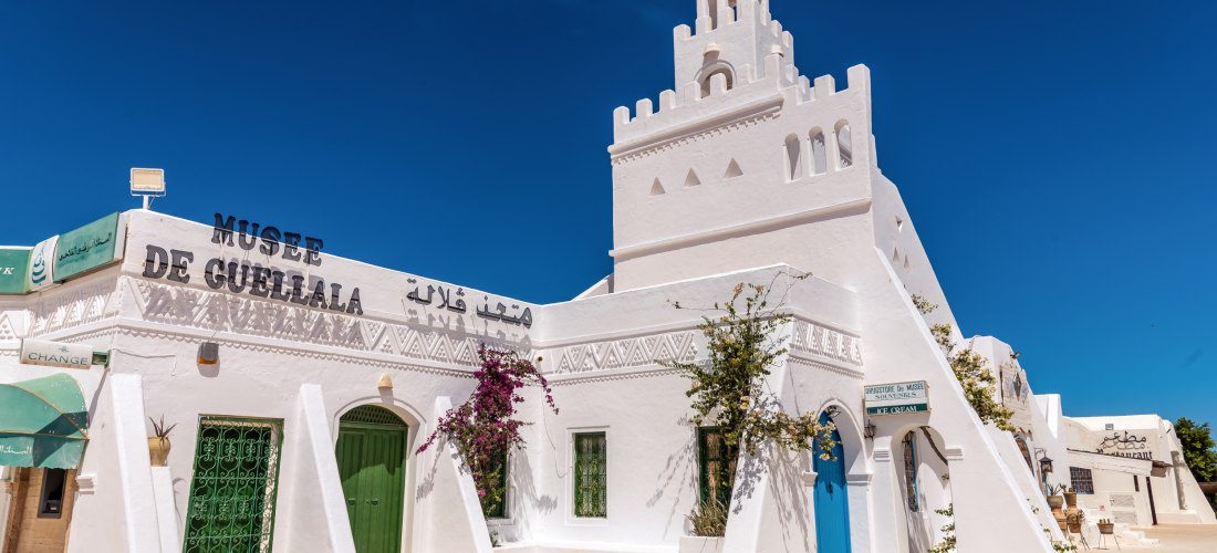 Das Musée de Guellala auf Djerba in Tunesien. Das strahlend weiße Gebäude mit grünen und blauen Türen ist mit traditionellen Ornamenten verziert und von Bougainvillea geschmückt. Ein blauer Himmel bildet den perfekten Hintergrund.