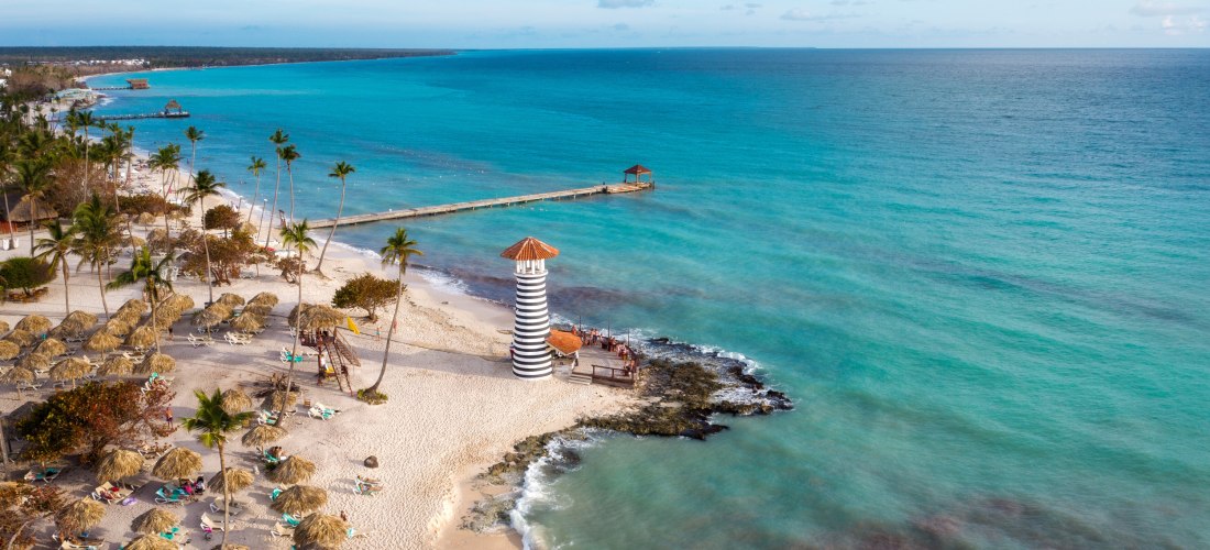 Strand mit schwarz-weiß gestreiftem Leuchtturm, weißem Sand und türkisblauem Meer in der Dominikanischen Republik