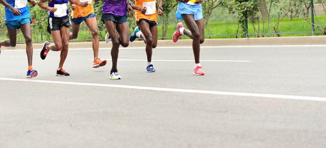 Gruppe von sechs Läufern in bunter Laufkleidung beim Marathon auf einer städtischen Straße. Nur Beine und Unterkörper sind im Bild, alle befinden sich im Laufschritt