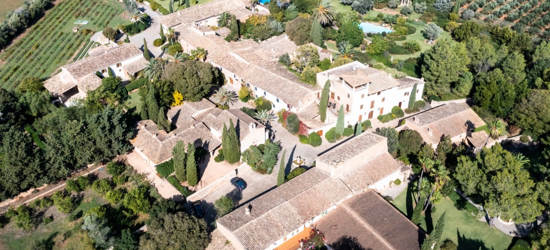 Luftaufnahme eines historischen mallorquinischen Landguts mit Garten, Olivenhainen und mehreren Gebäuden mit Terrakottadächern.