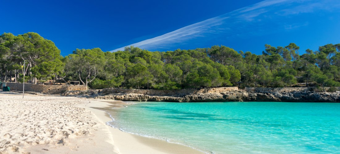 Strand von Cala Mondrago auf Mallorca, türkisblaues Wasser, blauer Himmel und Sonnenschein, üppige Vegetation im Hintergrund