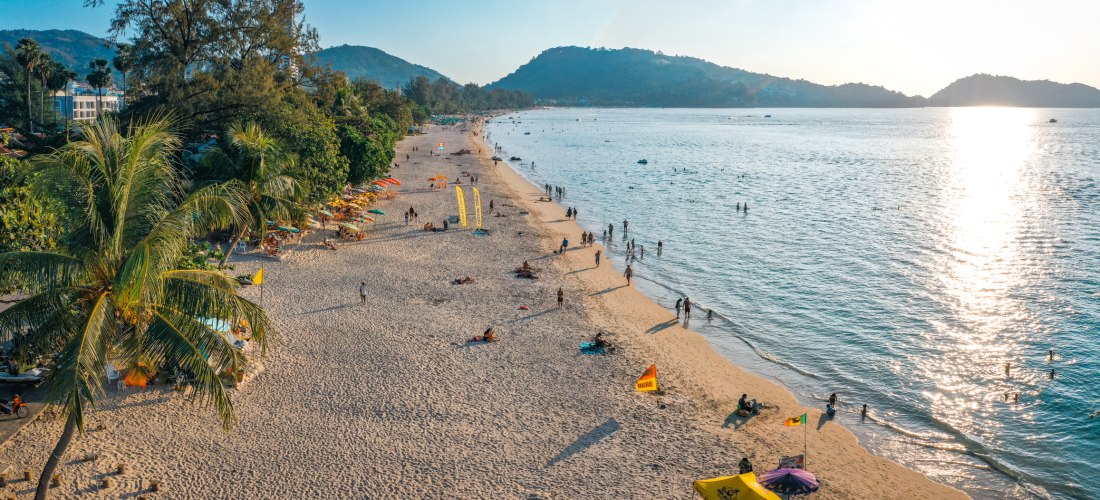 Tagesaufnahme vom Patong Beach auf Phuket mit feinem Sand, Palmen und badenden Urlaubern – beliebtester Strand auf Phuket 2025/2026