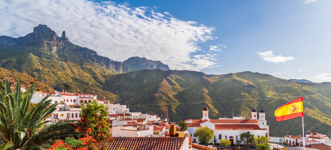 Blick auf das Bergdorf Tejeda auf Gran Canaria mit roten Ziegeldächern, spanischer Flagge und eindrucksvollen Bergen im Hintergrund.