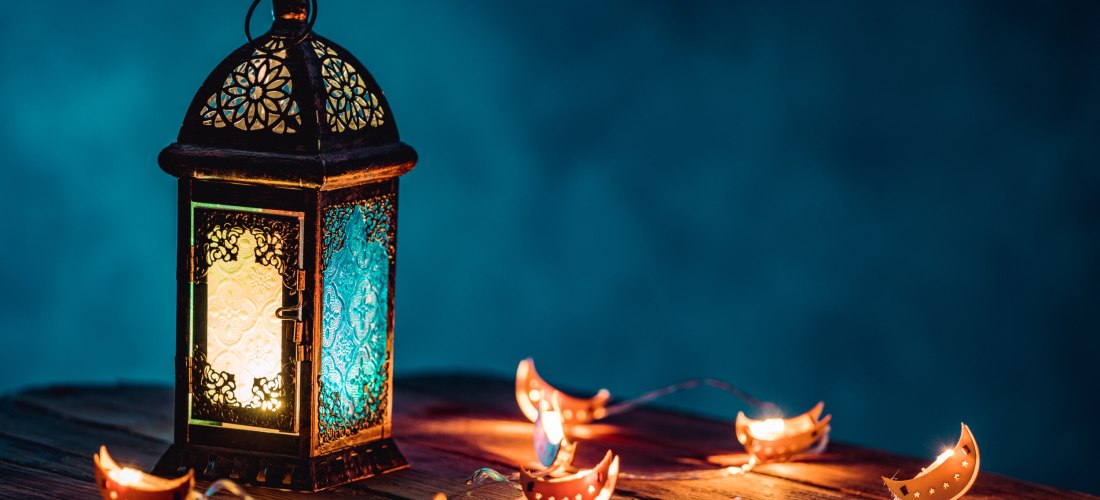 Eine orientalische Laterne mit buntem Glas leuchtet auf einem Holztisch, umgeben von dekorativen Lichterketten mit Mond- und Sternmotiven