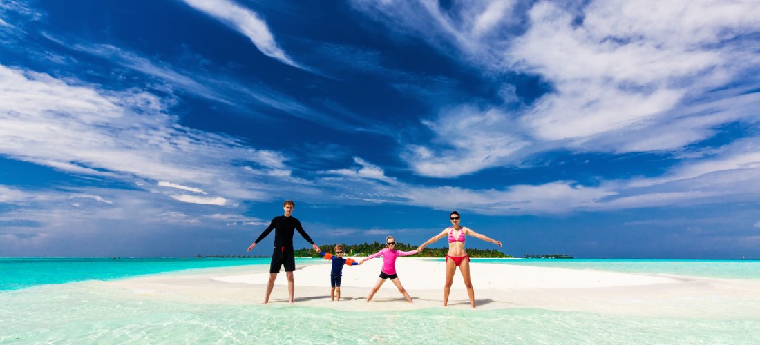 Eine Familie genießt ihren Urlaub auf einer traumhaften Sandbank mit kristallklarem Wasser und einem strahlend blauen Himmel. Ein perfekter Moment für unvergessliche Erinnerungen.