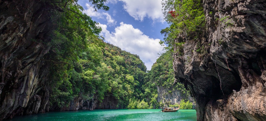 Lagune bei Krabi in Thailand mit smaragdgrünem Wasser, Karstfelsen und traditionellem Longtail-Boot.