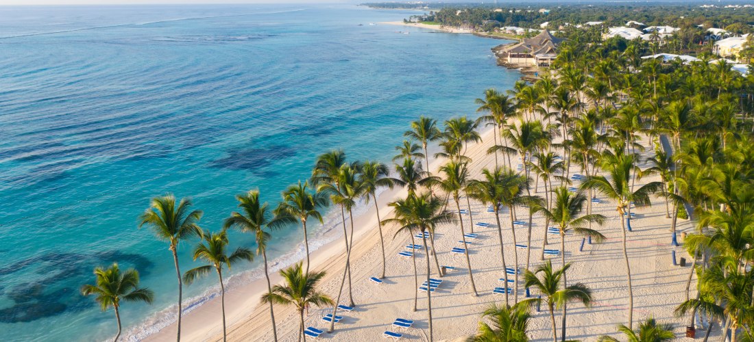 Weißer Sandstrand in Punta Cana mit Palmen, Sonnenliegen und türkisblauem Meer in der Dominikanischen Republik