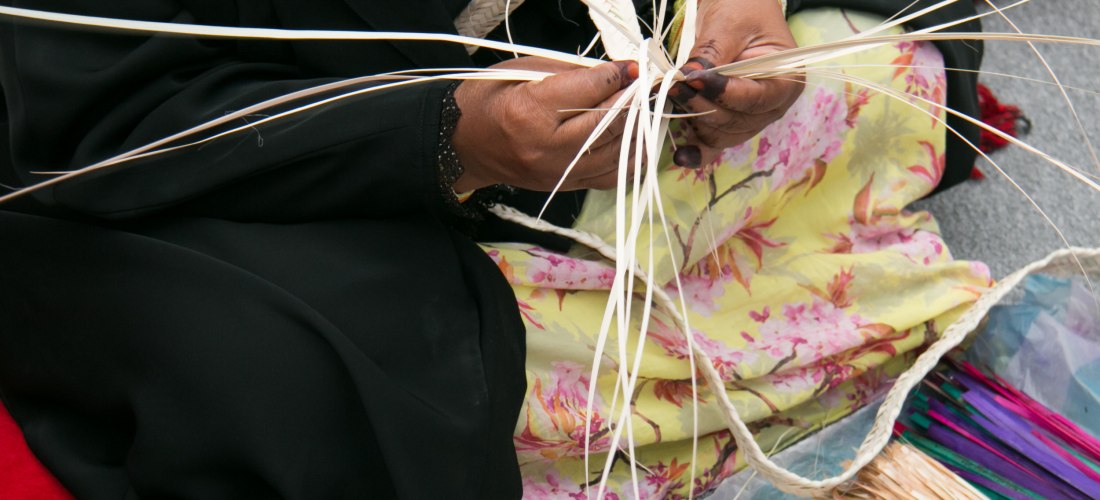 Nahaufnahme einer Frau in traditioneller Kleidung, die mit gewebten Palmblättern kunstvolles Flechtwerk herstellt