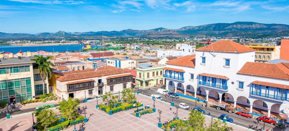 Parque Céspedes – Herzstück von Santiago de Cuba mit Kolonialarchitektur Blick auf den zentralen Parque Céspedes in Santiago de Cuba mit dem Ayuntamiento, kolonialen Gebäuden, Palmen und dem Meer im Hintergrund – beliebter Treffpunkt im Stadtzentrum.